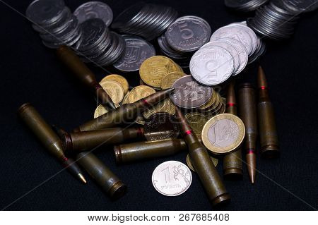 One Euro, Russian Ruble And Small Ukrainian Coins With Rifle Military Ammo On Black Background. Symb