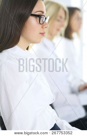 Attractive Businesswoman At Meeting Or Conference Against The Background Of Colleagues. Group Of Bus