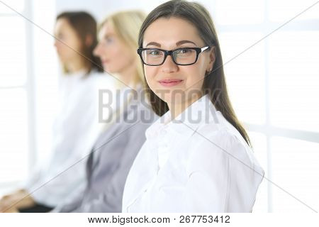 Attractive Businesswoman At Meeting Or Conference Against The Background Of Colleagues. Group Of Bus