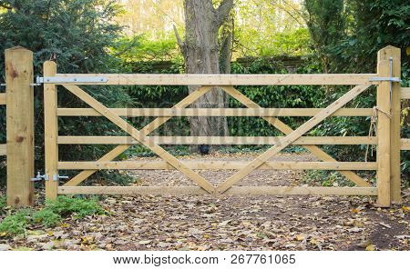 A Five Bar Wooden Gate Goes Through A Fence Leding Onto A Path Through A Wood