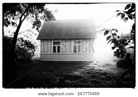 Small rural wooden house and spider web gossamer in the foggy morning. Vintage photography imitation.                           