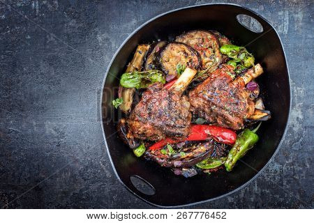 Traditional barbecue leg of lamb with eggplant and chili as top view in a modern style Japanese cast-iron roasting dish with copy space left