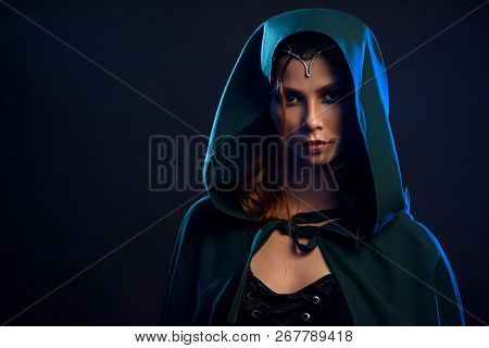 Portrait Of Young Charming Girl In Black Dress And Emerald Cloak With Hood On Her Head. Close Up Of 