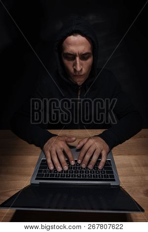Focused Hacker In Black Hoodie Using Laptop At Wooden Tabletop, Cuber Security Concept