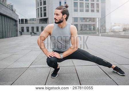 Picture Of Young Man Stratching His Leg And Warming Up. He Does Small Exercises For Legs. Guy Looks 