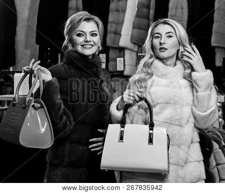 Girls With Smiling Faces In Black And White Fur Coats Hold Purses In Hands. Luxury Style Concept. Wo