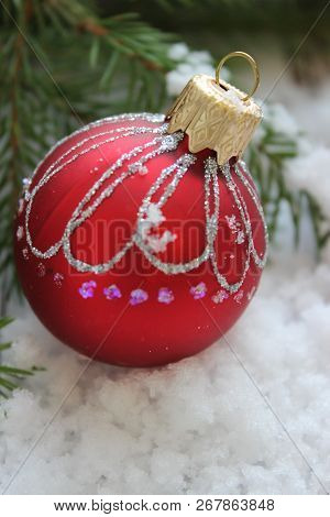 Christmas Card, Close-up Christmas Toy Red Ball With Shiny Pattern On The Snow Surrounded By Fir Bra