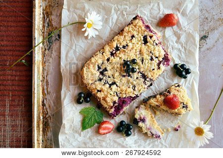 Top View Of Black Currant, Strawberry And Cottage Crumble Cake On Baking Paper And Rustic Background