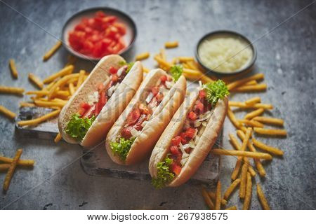 Assortment of three tasety hot dogs, placed on wooden cutting board. Served with french fries, onion and tomato. View from above. Stone background.