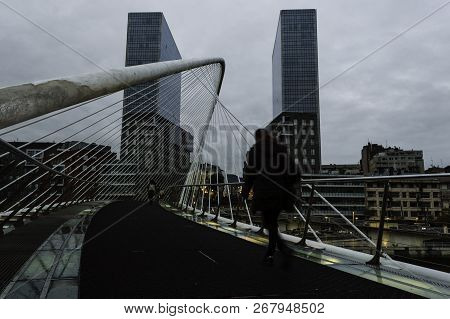 View Of A Zubizuri Bridge Over The Nervion River, With Pedestrians Walking On Their Way To Their Job