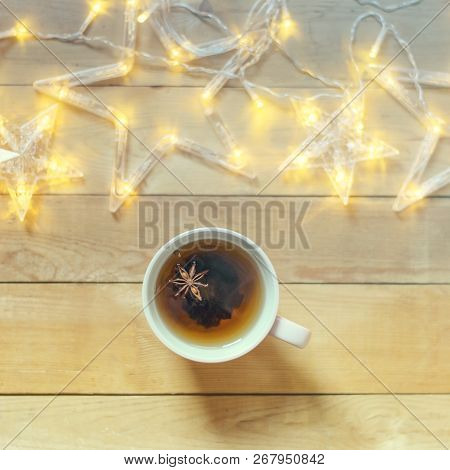 A Mug Of Hot Tea With Spices On A Wooden Background With Christmas Garland.flat Lay