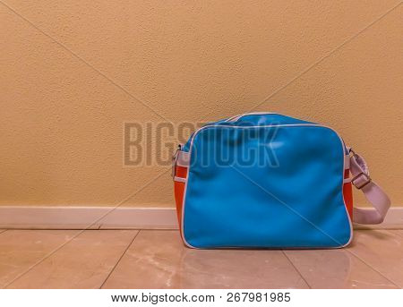 Blue With Red Messenger School Bag Isolated In Against A Wall And Standing On The Floor In A Room