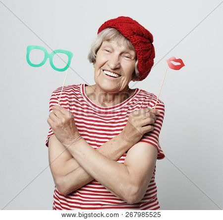 lifestyle, people and party concept: funny grandmother wearing red clothes holding falce glasses and  ready for party