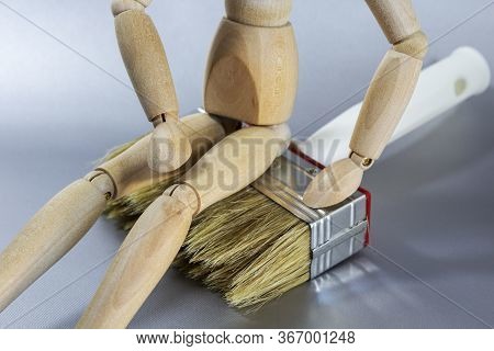 Close Up Of A Wooden Doll With Her Hand On Her Thigh, Sitting On A Brush