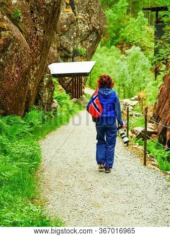 Tourist Woman With Norwegian Flag And Camera Walking Trough Mountains Path In Allmannajuvet Area Sau