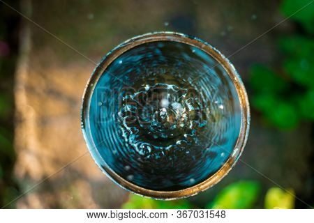 Top View Of Water Leaking From A Tap Into Round Container Outdoors Garden. Selective Focus