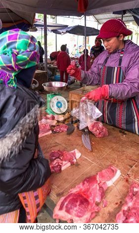 Bac Ha, Vietnam, January 7, 2020 - Butcher at Bac Ha Market saling raw meat on her wooden dark table