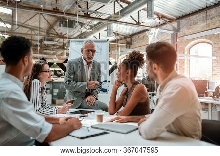Business Meeting. Mature Businessman Explaining Something To His Colleagues While Sitting At The Off