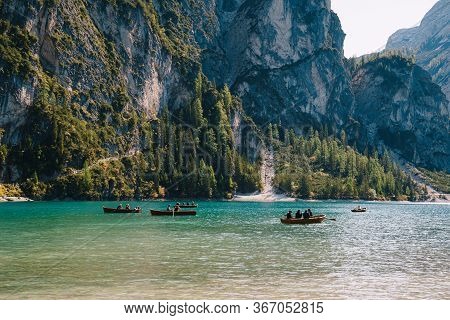 Tourists Swim In Wooden Boats On The Lago Di Braies Amid Rocky Mountains And Forests. Braies Lake In