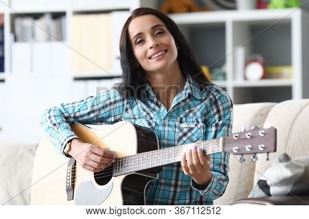 Woman Sitting At Home On Sofa And Playing Guitar. Online Music Lessons During Quarantine. Private Le