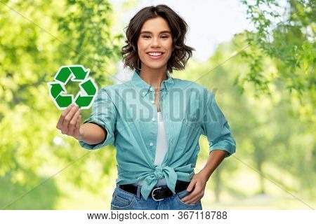 eco living, environment and sustainability concept - portrait of happy smiling young woman in turquoise shirt holding recycling sign over green natural background