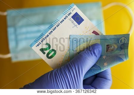 Gloved Hands Hold A Twenty-euro Bill Against A Background Of Medical Masks. The Concept Of Scarcity 
