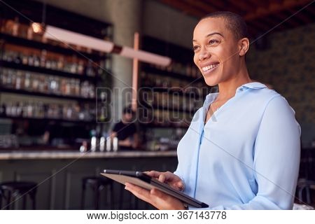 Confident Female Owner Of Restaurant Bar Standing By Counter Holding Digital Tablet