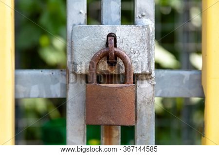 A Closed Rusty Steel Padlock Frame On A Metal Reinforcement Closeup, Frontal Shot. Safety And Securi