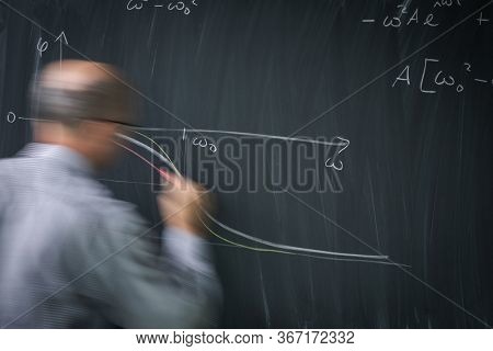 Math teacher drawing   fuction graph on a blackboard during mathclass (motion blurred image)