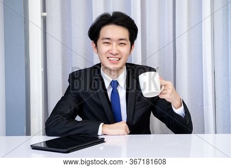 Asian Business Man Dringking Coffee Wearing Suit, Enjoying Watching Educational Webinar On Laptop Or