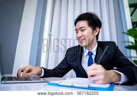 Asian Business Man Dringking Coffee Wearing Suit, Enjoying Watching Educational Webinar On Laptop Or