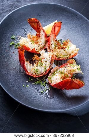 Traditional barbecue spiny lobster tail sliced and offered with lemon slice and herbs as closeup on a modern design plate 
