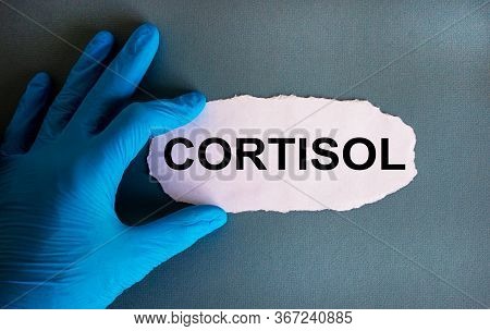 Hand In Blue Glove With White Small Paper. Concept Word 'cortisol'. Blue Background.