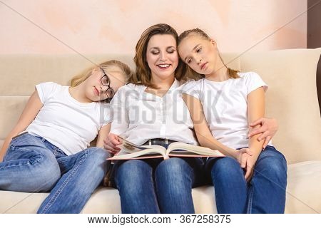 Home Staying Time. Portrait Of Young Caucasian Mother Reading A Book Together With Her Twin Daughter