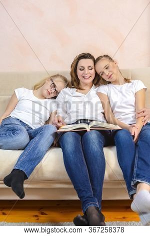 Home Staying Time. Portrait Of Young Caucasian Mother Reading A Book Together With Her Twin Daughter