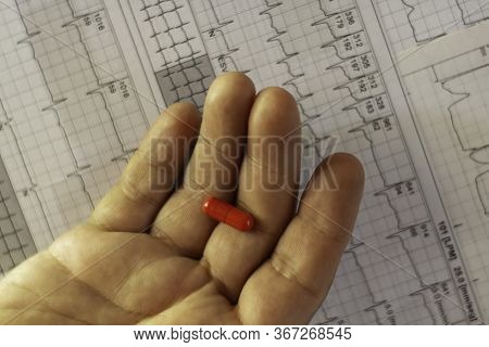 Hands Of A Man Holding A Red Capsule On An Electrocardiogram. Medicines For The Heart.