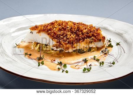 Baked cod fillet with sauce. Restaurant food portion side view. Fish with batter garnish served on white craft plate. Seafood sprinkled with breadcrumbs meal course. Luxury gourmet dish serving