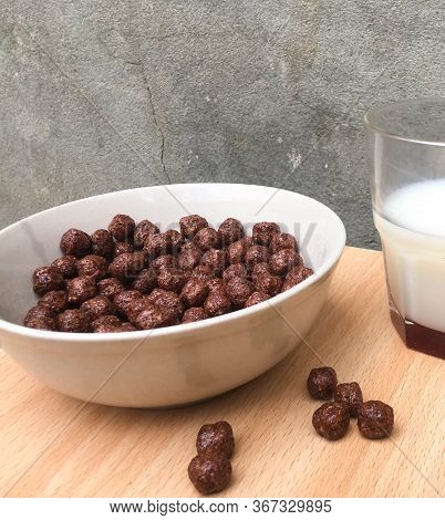 Bowl With Chocolate Balls And A Cup Of Milk On A Wooden Table. Sweet Cocoa, Chocolate, Sugar, Cereal