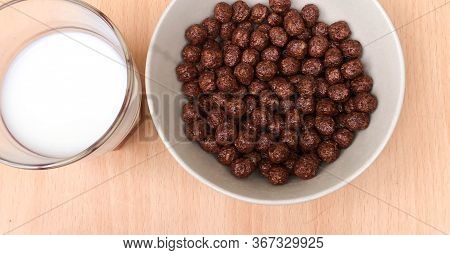 Bowl With Chocolate Balls And A Cup Of Milk On A Wooden Table. Sweet Cocoa, Chocolate, Sugar, Cereal