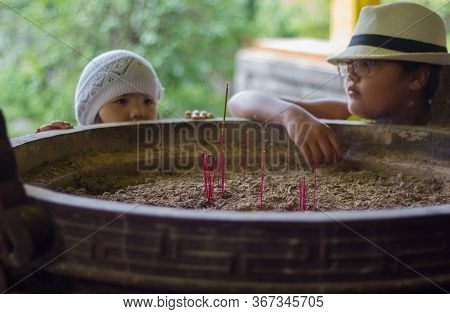 Girls Look At Red Candles In A Large Vase Of A Buddhist Temple