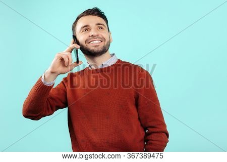 Gleeful Bearded Young Man In Casual Outfit Talk On Smartphone Over Cyan Background.
