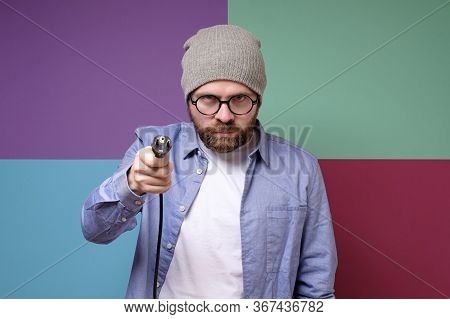 Angry Bearded Man, In Round Glasses And A Hat, Holds In Hands An Electric Plug With A Cord.