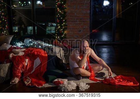 Bad Santa Claus On The Background Of Christmas Decorations. A Man In A Suit Of Santa Claus After The