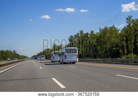 Four New White Minibuses Ride In A Convoy Along The Highway On A Sunny Day In Summer. Back View