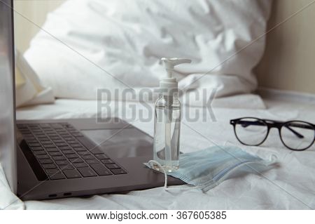 Laptop, Glasses, Face Mask And Sanitaizer On A Bed In A White Bedroom.work From Home Concept