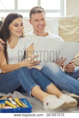 Young couple moving in to new home together, sitting on The floor and diskuss plan of desing.