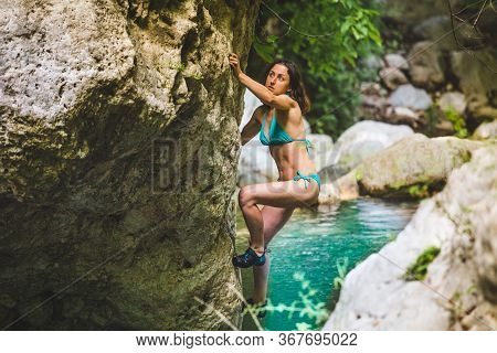 A Woman In A Swimsuit Climbs A Cliff Above The Water, Climbing Over A Mountain River, Bouldering In 