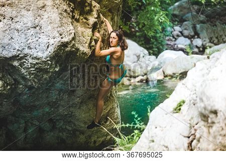 A Woman In A Swimsuit Climbs A Cliff Above The Water, Climbing Over A Mountain River, Bouldering In 