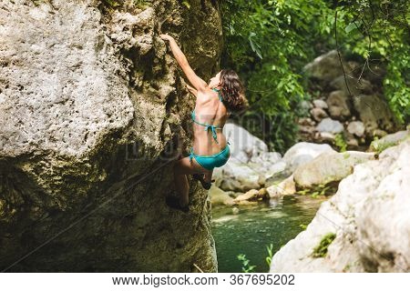 A Woman In A Swimsuit Climbs A Cliff Above The Water, Climbing Over A Mountain River, Bouldering In 