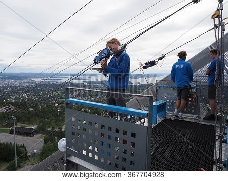 Oslo, Norway On July 2019: Three Young Men Care About Zipline Rider In European City Seen From Ski J